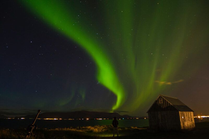 Aurora boreal verde sobre el horizonte y una pequeña cabaña de madera en la costa de Islandia. Aurora boreal verde sobre el horizonte y una pequeña cabaña de madera en la costa de Islandia.