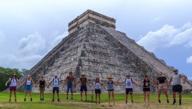 viajeros de weroad saltando dándose la mano delante de la pirámide de chichen itza en méxico