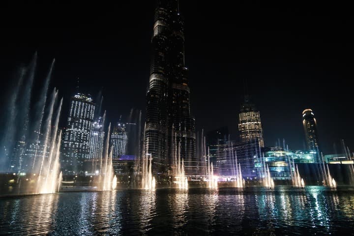 espectáculo nocturno de fuentes delante de un rascacielos en dubái - weroad