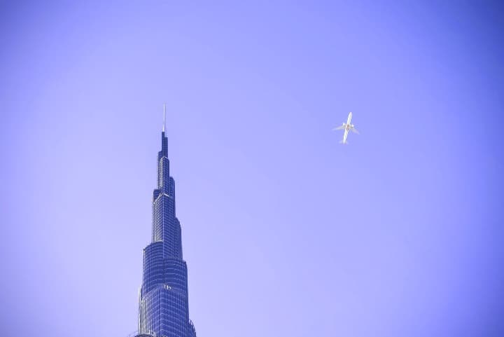 punta del rascacielos burj khalifa, detrás cielo azul y avión que pasa al lado - weroad
