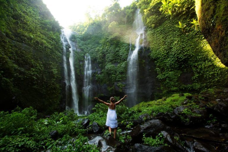 chica de espaldas vestida de blanco con brazos levantados delante de las cascadas de sekumpul - weroad