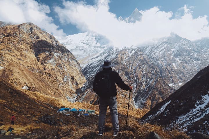 persona con sobrero y bastones, de espaldas, en medio de una montaña en ghandruk, algo que ver en nepal - weroad