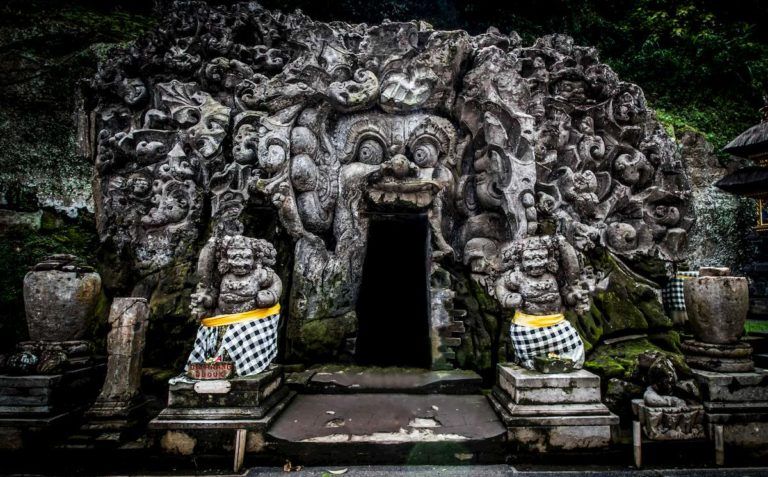 entrada del templo de goa gajah en bali, dos estatuas tienen un telo de color blanco, negro y amarillo - weroad