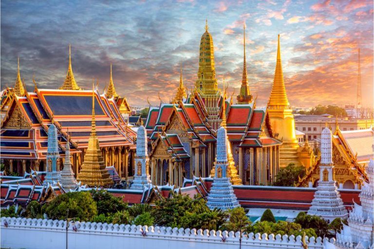 gran palacio de bangkok visto desde la distancia, se aprecian edificios y cielo rosado detrás - weroad