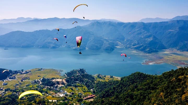 paracaidas ram air volando con el fondo el paisaje verde y con un lago en pokhara, nepal - weroad