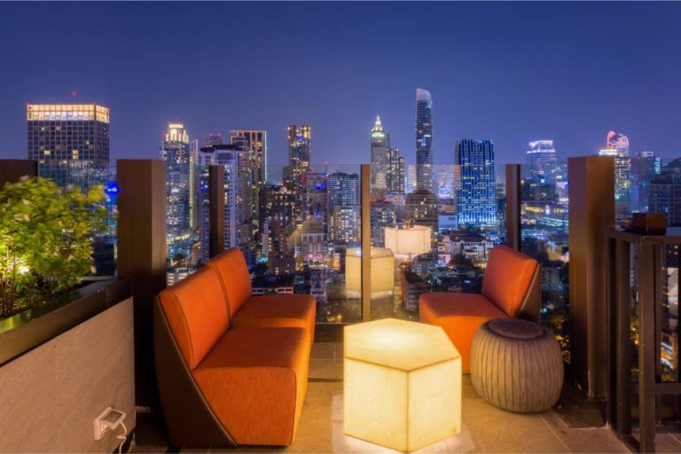 sky bar, sofas color naranja con delante una mesa iluminada, al fondo el skyline de la ciudad con sus rascacielos - weroad