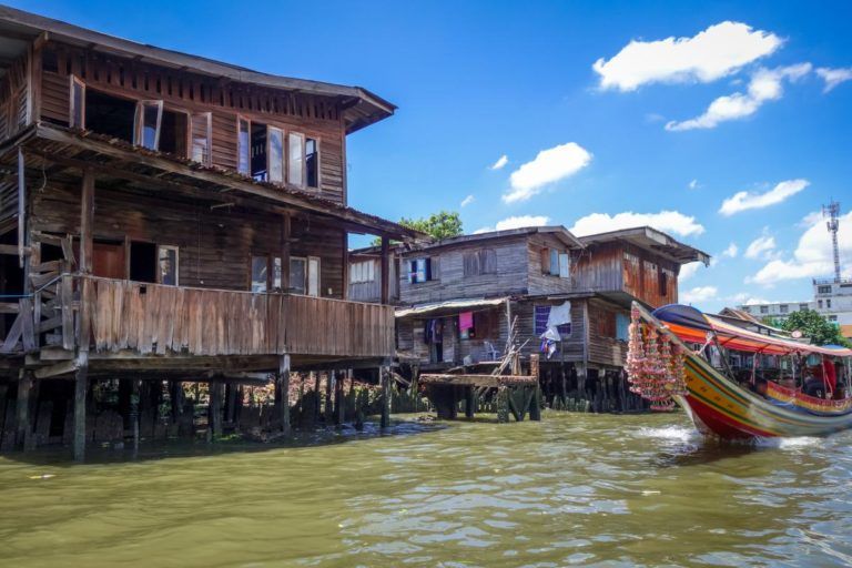 casas de madera en medio dell agua en thonburi, un barco colorido pasando delante - weroad