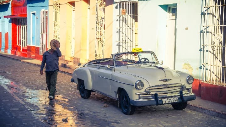 coche descapotable antiguo y hombre que pasea al lado quitándose el sombrero en trinidad - weroad