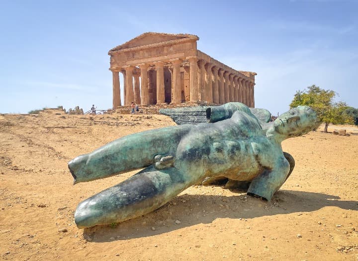 estatua en bronce de icaro caido con detrás uno de los templos de agrigento, sicilia - weroad