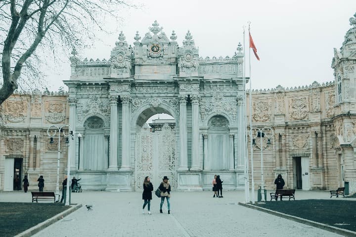 exterior del palacio blanco de dolmabahçe, se aprecia un portal y algunas personas paseando delante - weroad