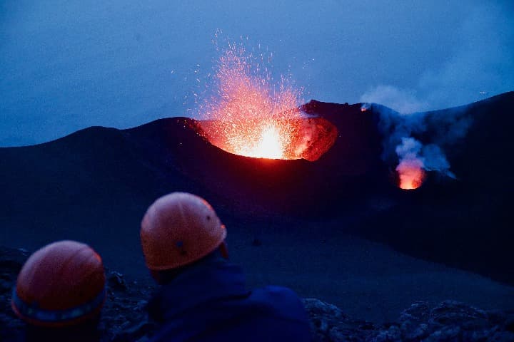 vulcan de stromboli eruptando, delante las cabezas de dos personas con casos, detrás el cielo azul - weroad