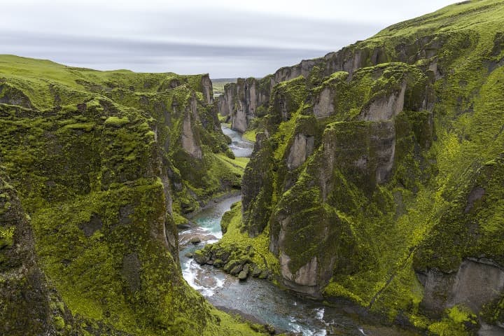 fiordo en fjaðrárgljúfur, islandia, rodeado de altas rocas cubiertas de verde - weroad