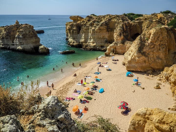 vista aere de una playa de algarve entre rocas, sombrillas y gente. vacaciones en portugal en agosto - weroad