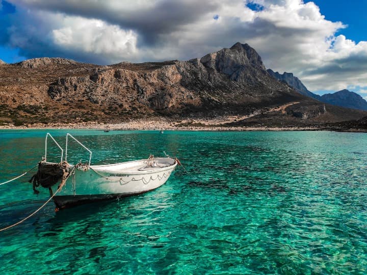 barco en agua verde en la playa de balos en creta, una de las islas de grecia. al fondo una montaña y cielo azul - weroad