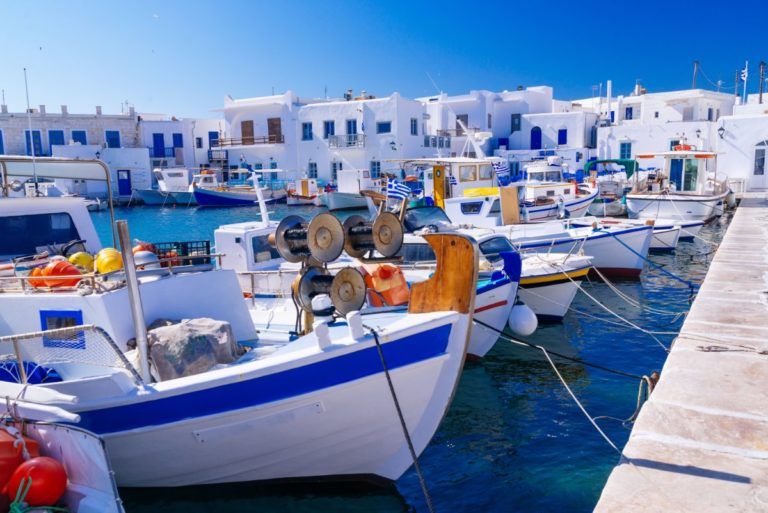barcos amarrados en el puerto de paros, una de las islas griegas, al fondo casitas blancas con puertas y ventanas azules - weroad