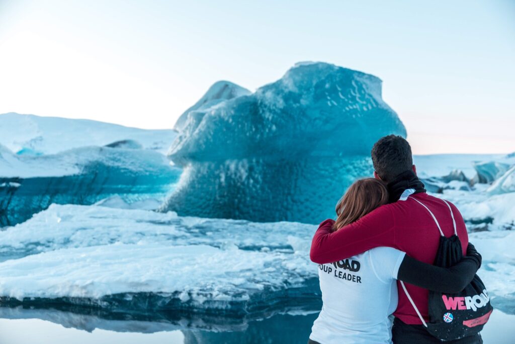 un chico y una chica abrazados de espaldas y con mochila de weroad miran un trozo de hielo inmersos en medio de la nieve