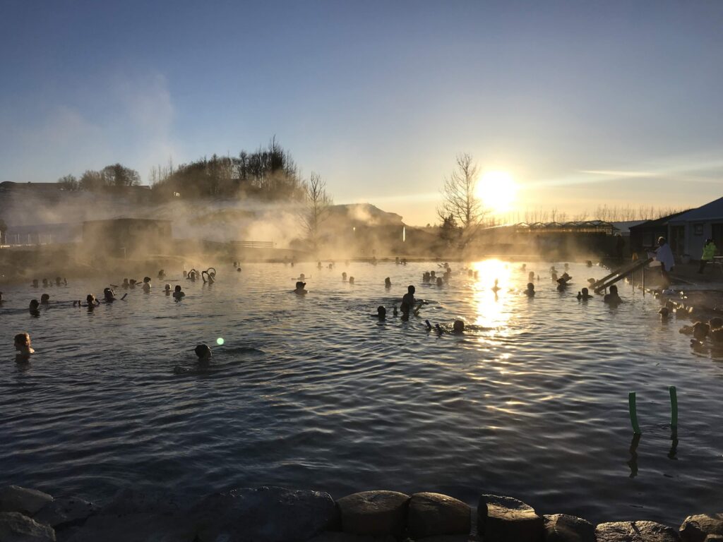 gente bañandose en una laguna con agua de la que sale humo, al atardecer - weroad