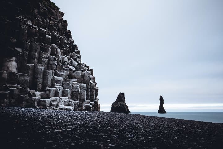 playa de arena negra en reynisfjara, algo que ver en islandia, al fondo el mar, una montaña negra - weroad