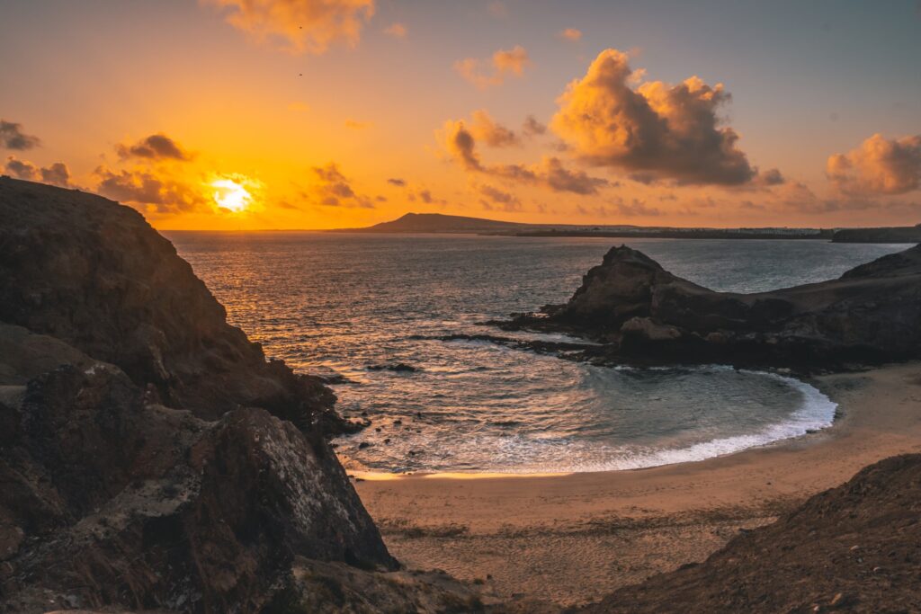 playa de lanzarote con rocas y arena y sol anaranjado detrás de las nubes - weroad
