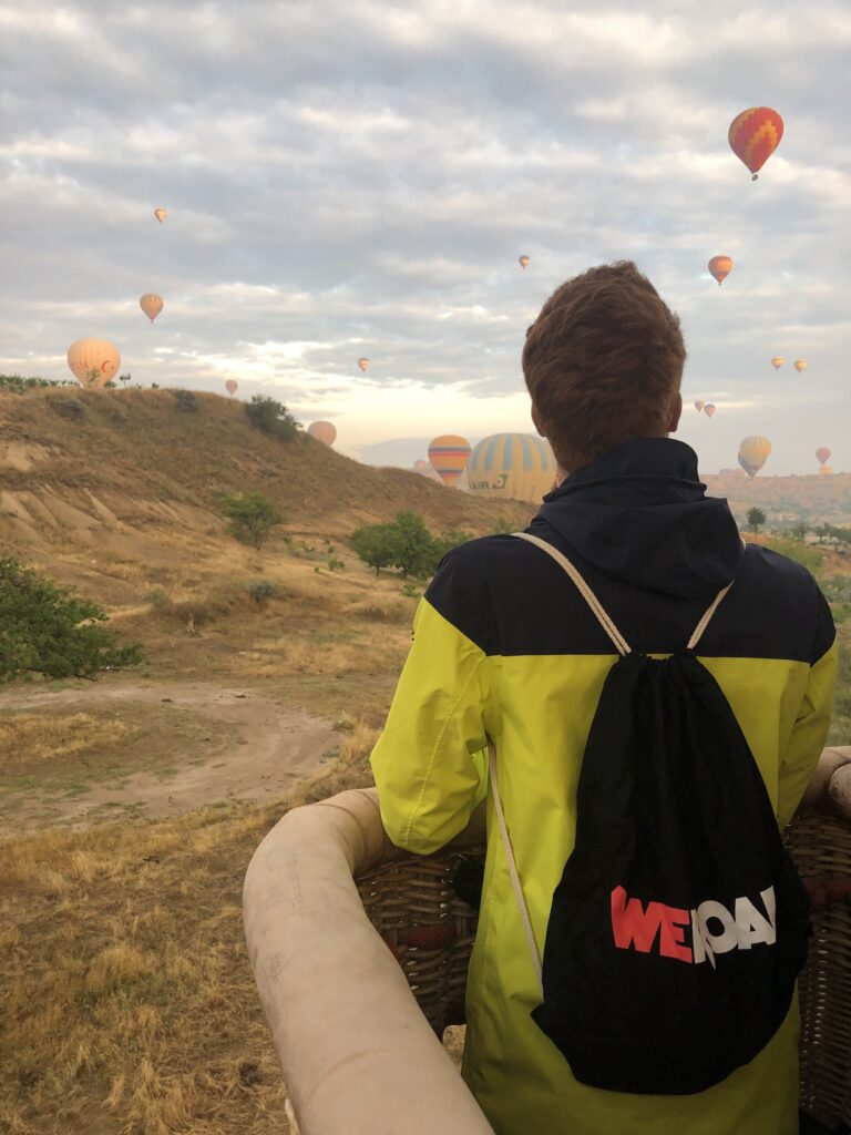 viajero con mochila weroad de espaldas en la cesta de un globo aerostático, en tierra. mira globos de colores volando en el cielo