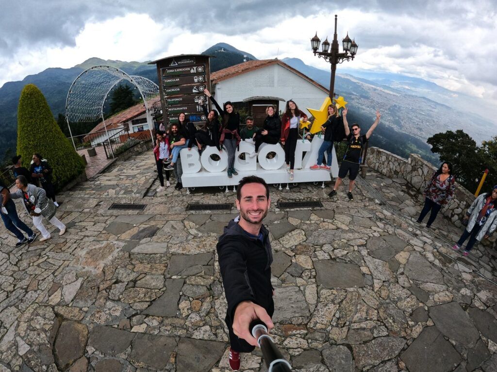 selfie de un viajero de weroad con detrás el grupo subido a la palabra bogotá, al fondo paisaje de la ciudad