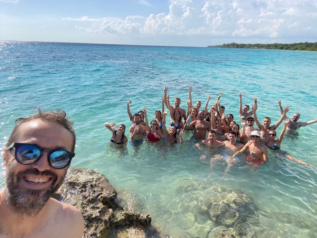 selfie por parte de un viajer de weroad con detrá sus compañeris de viaje metidos en el agua verde de una playa de cuba