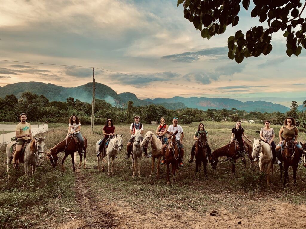viajeros de weroad montados en caballos en viñales, lugar que ver al viajar a cuba, detrás paisaje verde y cielo azulado