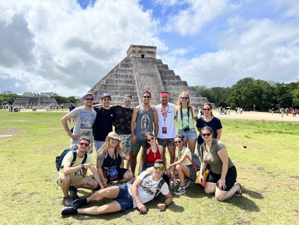grupo de viajeros weroad mirando a camara con detrás la pirámide de chichen itza en méxico, buen destino de vacaciones en agosto fuera de europa