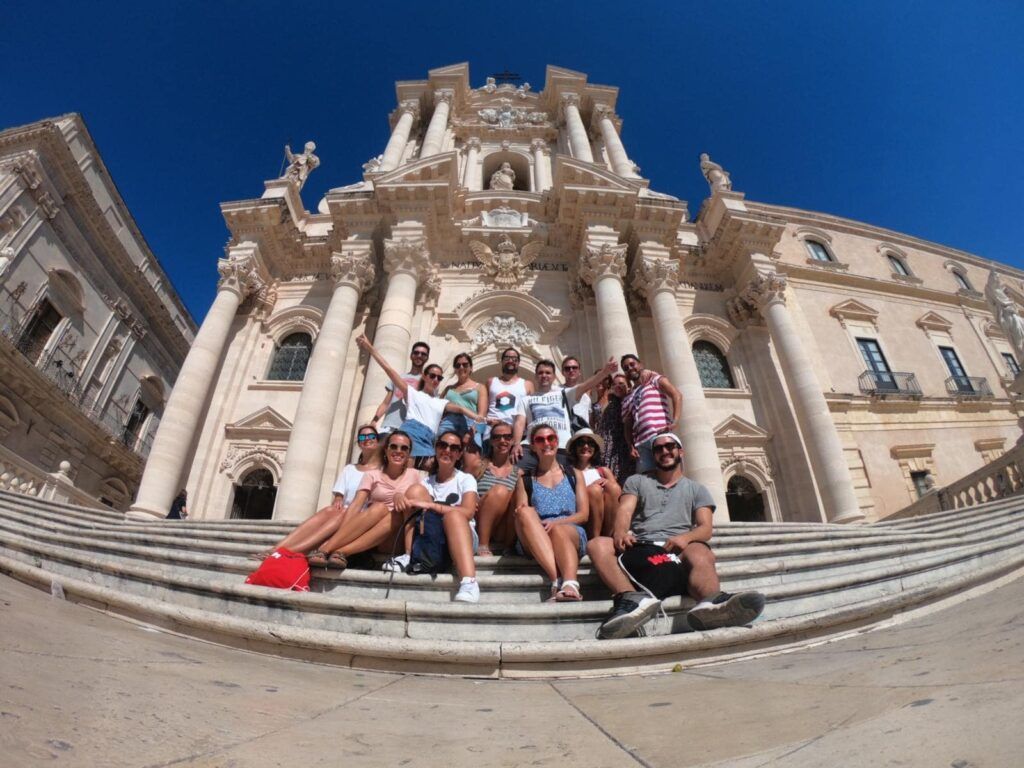 foto de grupo de viajeros de weroad sentados en las escaleras delante del duomo de siracusa, ciudad que ver en sicilia
