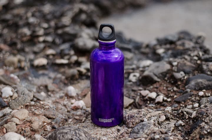 botella térmica de acero azul apoyada encima de una roca, un accesorio de viaje eco-friendly - weroad