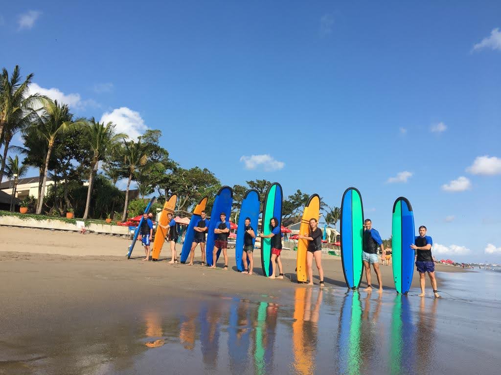 grupo de viajeros de weroad aguantando tabla de surf en la playa de kuta, indonesia