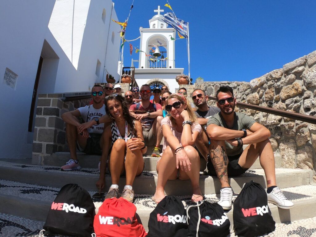 grupo de viajeros weroad sentados en unas escaleras con detrás la campana de una iglesia en kos, grecia