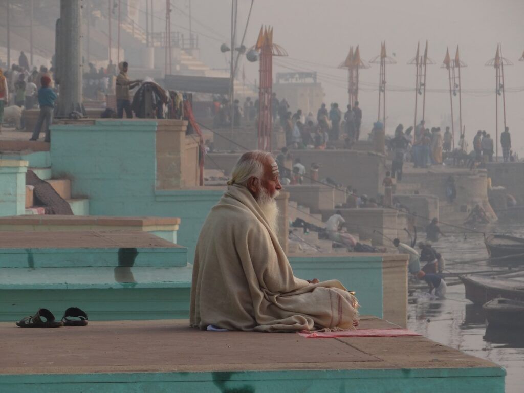 señor mayor sentado mirando el rio ganges en varanasi, en india, detrás moltitud de gente - weroad