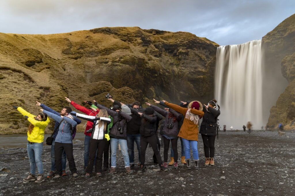 Grupo de viajeros weroad delante de una cascada de islandia tapándose la cara con el brazo