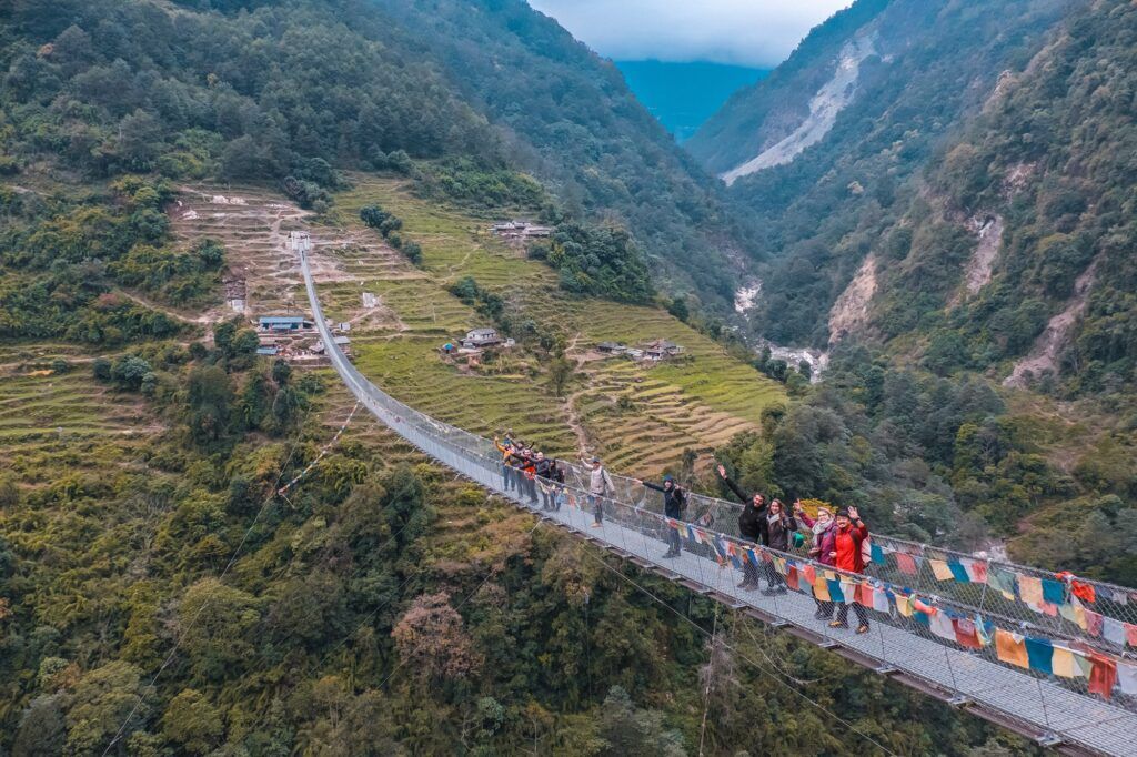 grupo de viajeros de weroad caminando por encima de un puente suspendido y con banderitas de colores en medio de la naturaleza de ghandruk, algo que ver en nepal