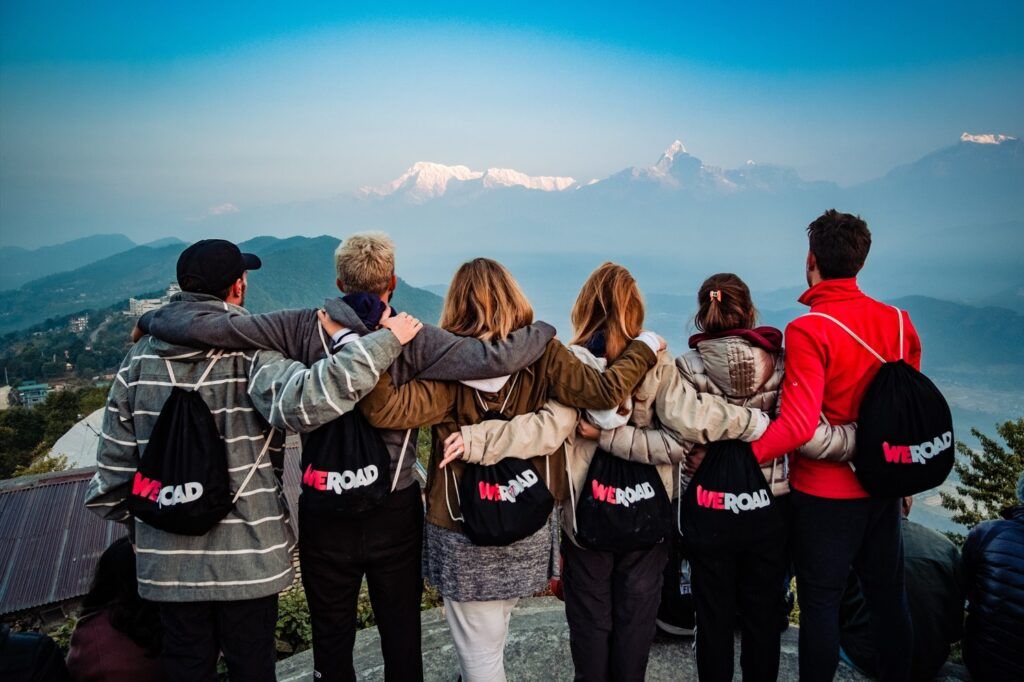 seis viajeros de weroad con sus mochilas corporativas, de espaldas, mientras miran las montañas que ver en nepal