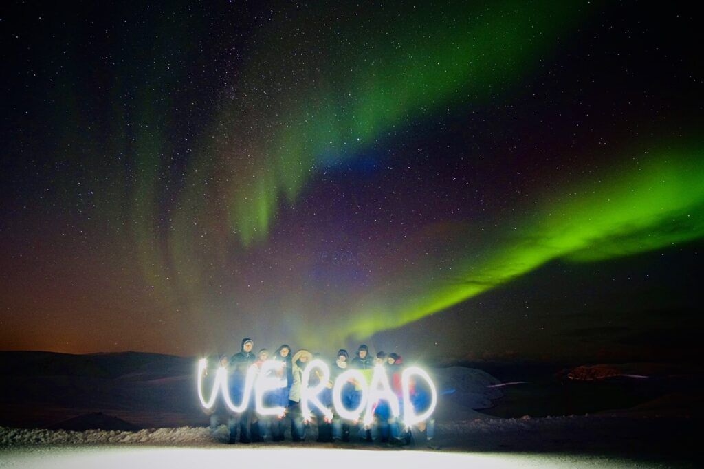 grupo de viajeros con delane la escrita weroad creada con luces, detrás aurora boreal en noruega
