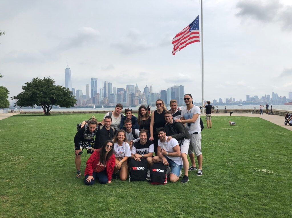grupo de viajeros de weroad delante de una bandera americana, al fondo los rascacielos de manhattan, nueva york