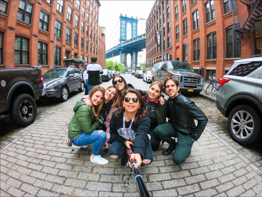 selfie de grupo weroad de cuclillas en una calle de brooklyn con detrás parte del puente, una de las cosas que ver en nueva york