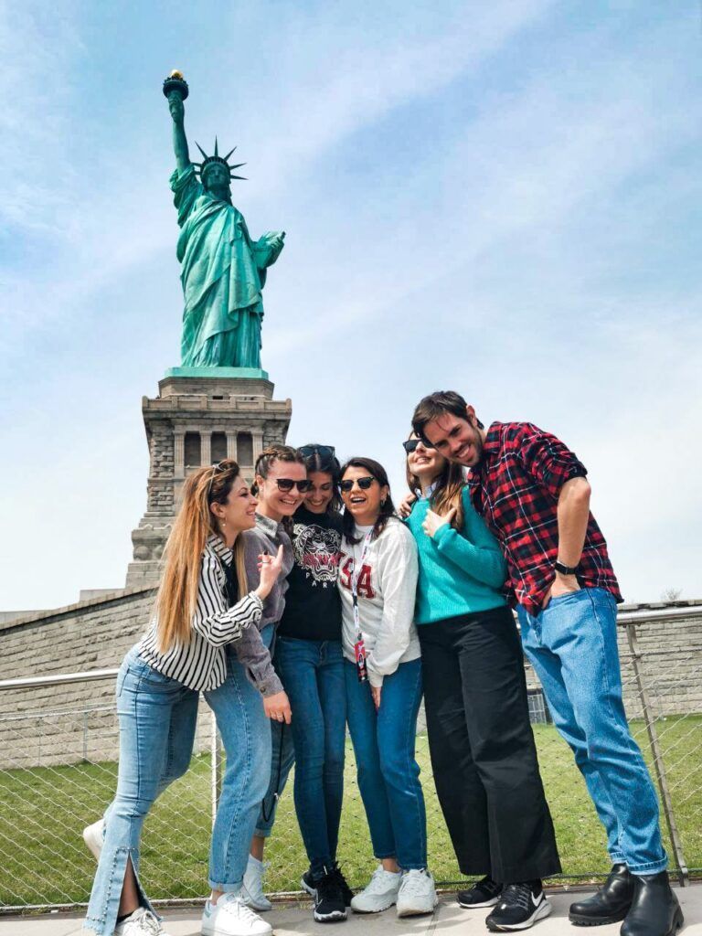 grupo de viajeros weroad de pie delante de la estatua de la libertad, una de las cosas que ver en nueva york