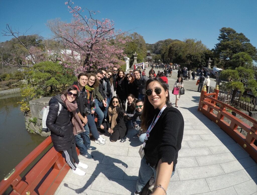 selfie de viajeros weroad encima de un puente en japón con detrás arbol de cerezo