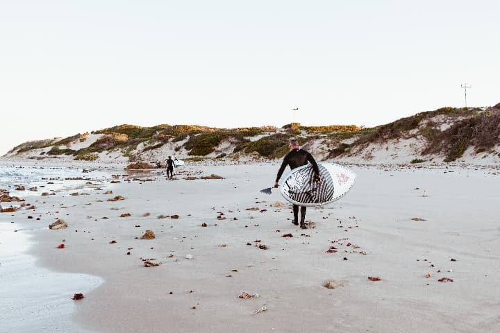 surfero de espaldas caminando por la orilla del mar aguantanto su tabla, sudafrica qué ver - weroad