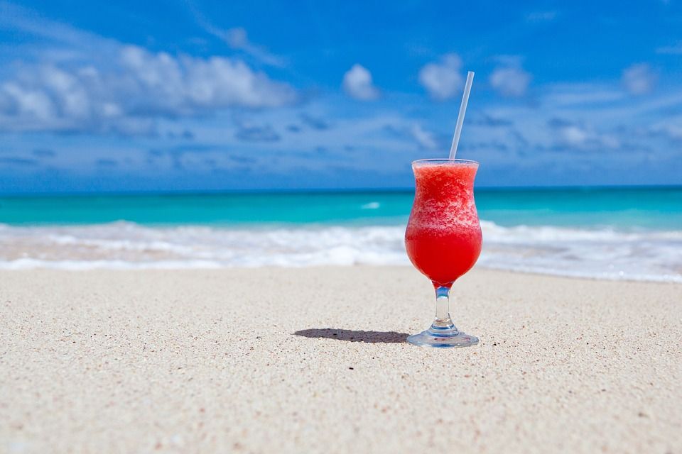 cocktail con pajita apoyado en la arena de una playa - weroad