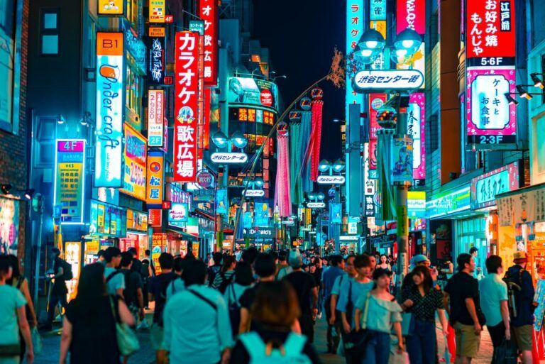 gente caminando en medio de calle iluminada por tiendas y carteles de neon con escritas en japonés - weroad