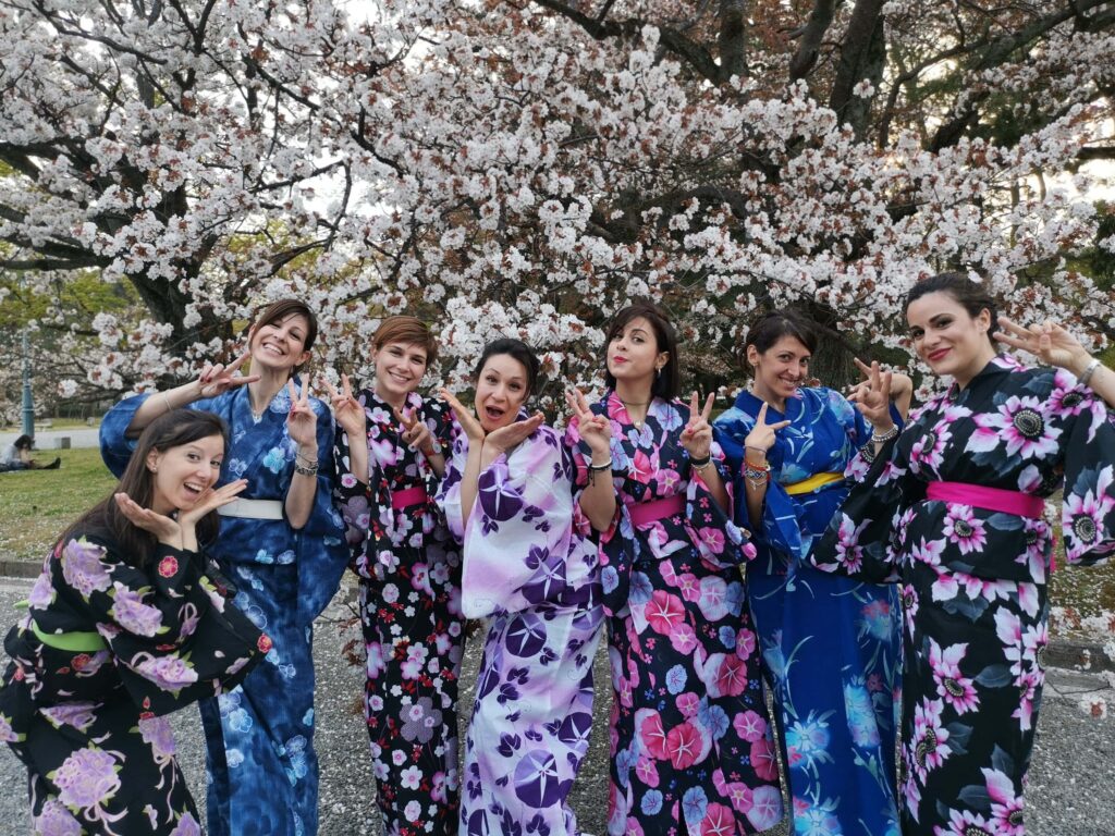 viajeras de weroad vestidas con kimono en japón, destino que visitar en los festivos 2023, detrás arboles e cerezo