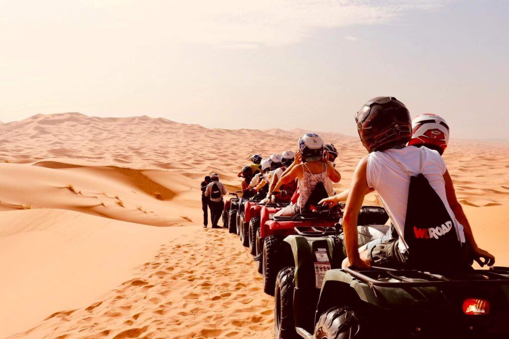 viajeros con mochilas weroad, de espaldas, montados en quad en el desierto de marruecos