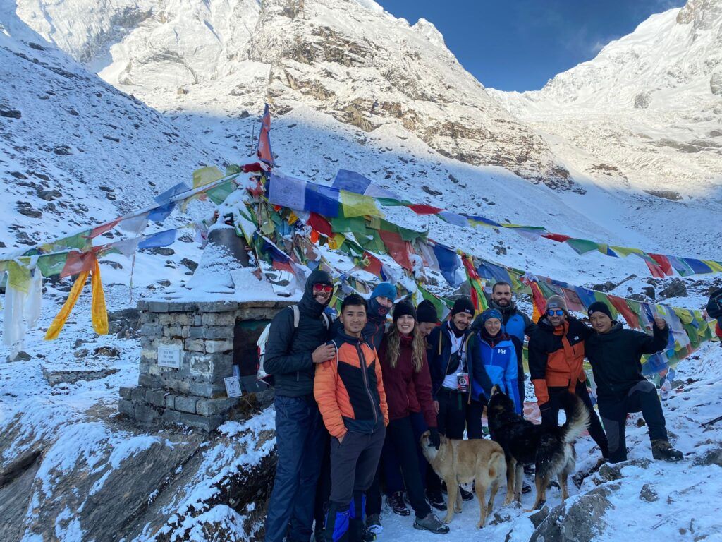 grupo de viajeros weroad y dos perros delante de una montaña con banerdas e colores durante un trekking en nepal, destino que visitar en los festivos 2023