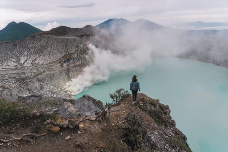 chica asumandose a la cumbre del volcán ijen en indonesia, humo saliendo del agua que conteiene - weroad