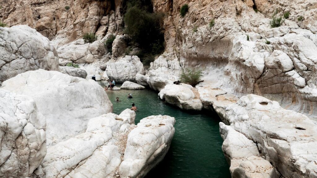 personas bañandose en agua entre rocas, el wadi bani khalid, algo que ver en oman - weroad