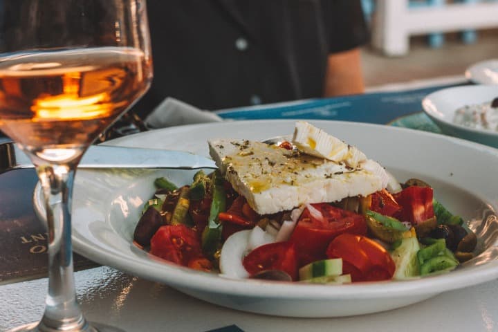 ensalada griega con queso feta encima, un vaso de vino en primer plano - weroad